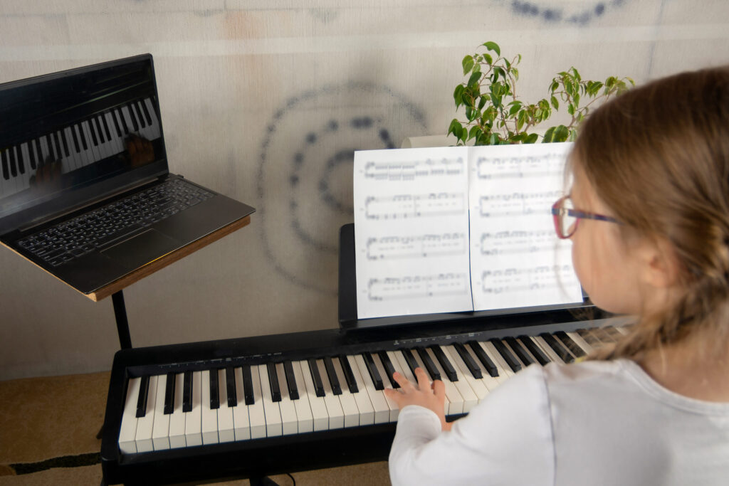 Girl learning to play the piano in distance learning via laptop over the Internet