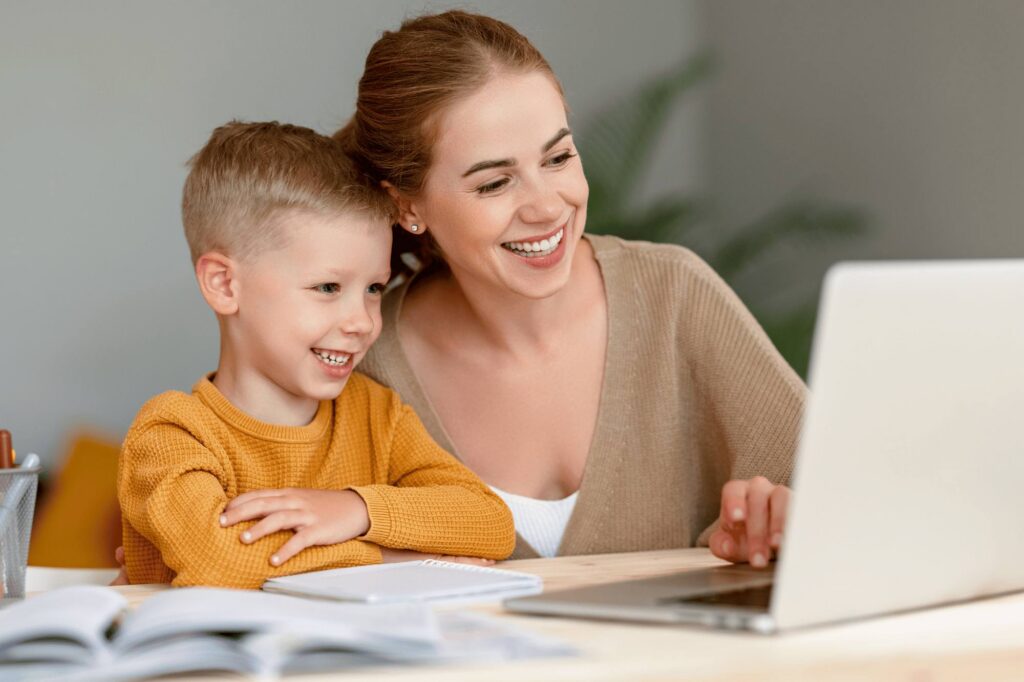 My child refuses to go to school: A happy child sitting next to his mother, studying online from home